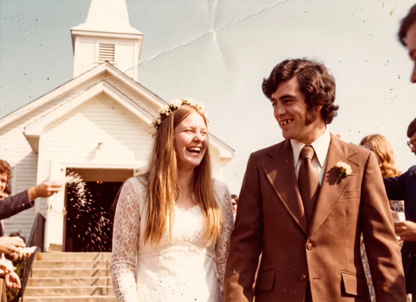 A laughing bride and groom leaving a white chapel under a shower of rice