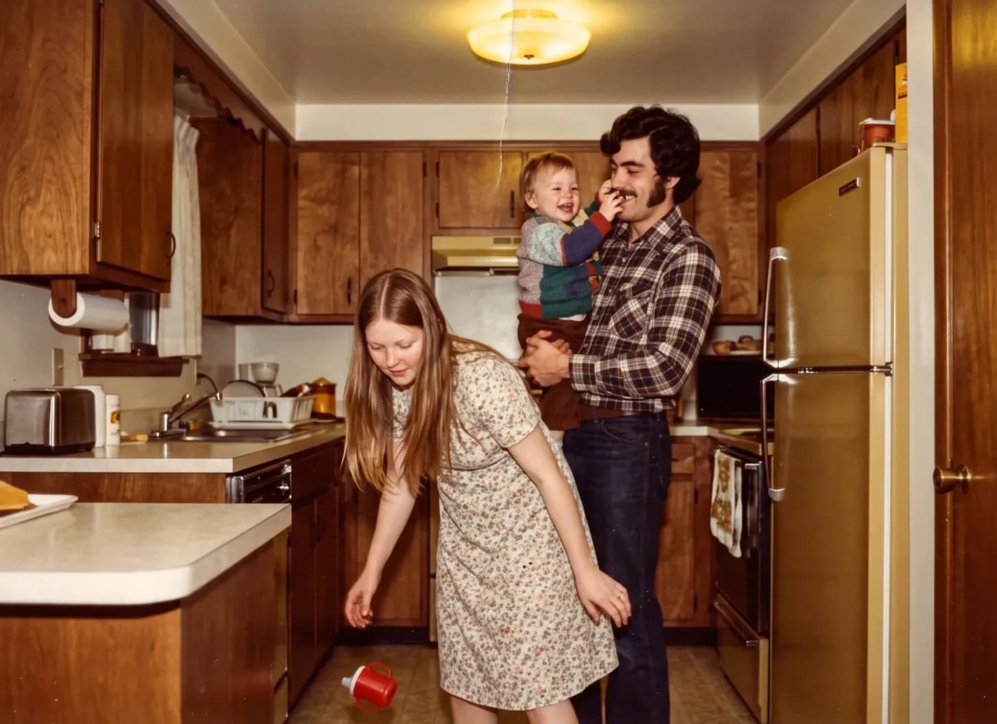 The young couple in a wood-paneled kitchen, the father holding their baby