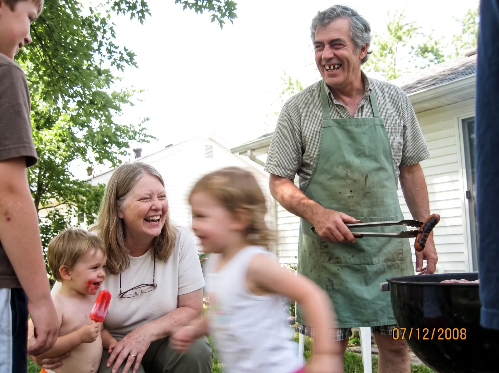 The couple, now grandparents, at a backyard barbecue with two small grandchildren