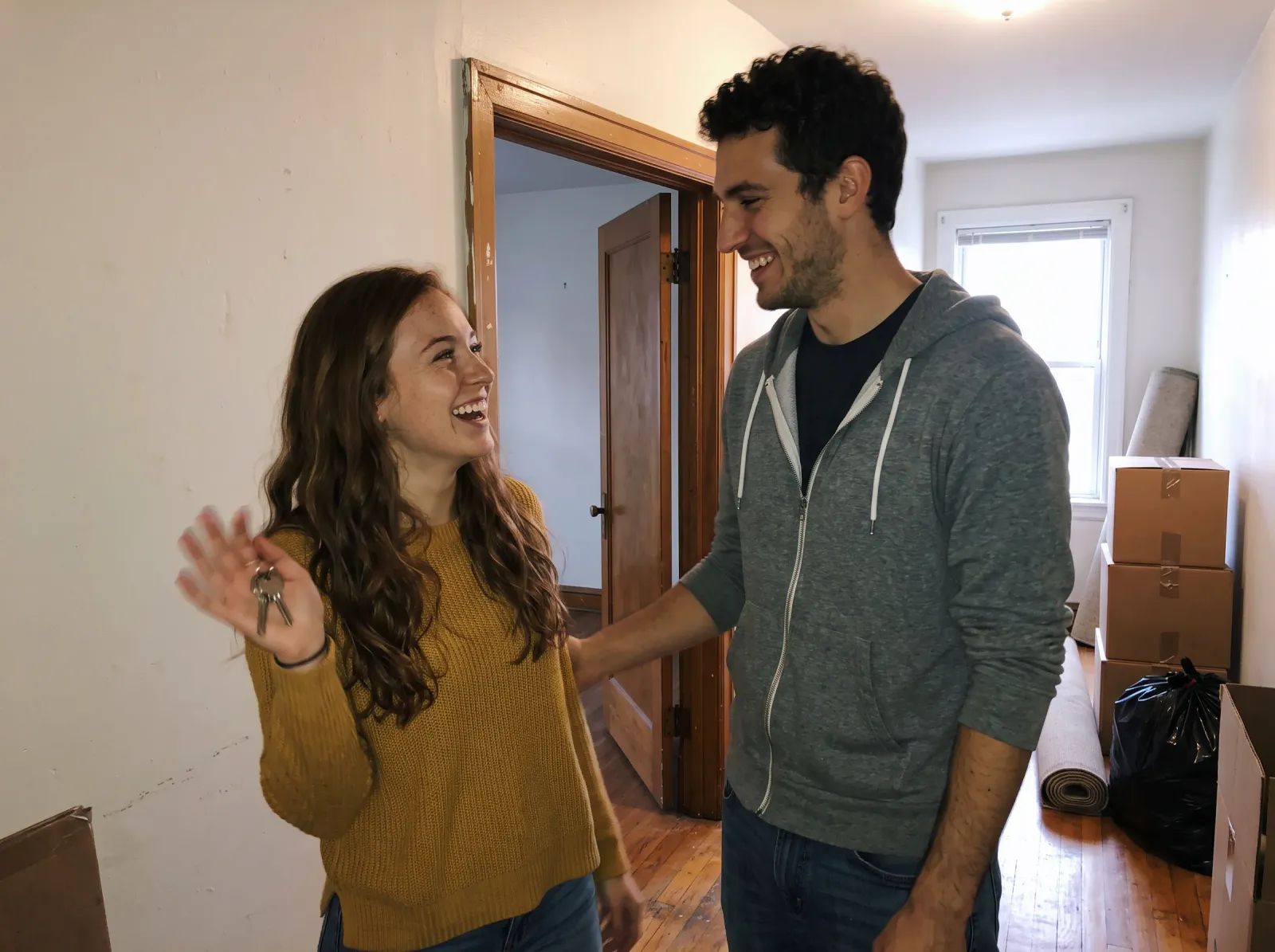 A young couple in an empty apartment, she holds up the new keys