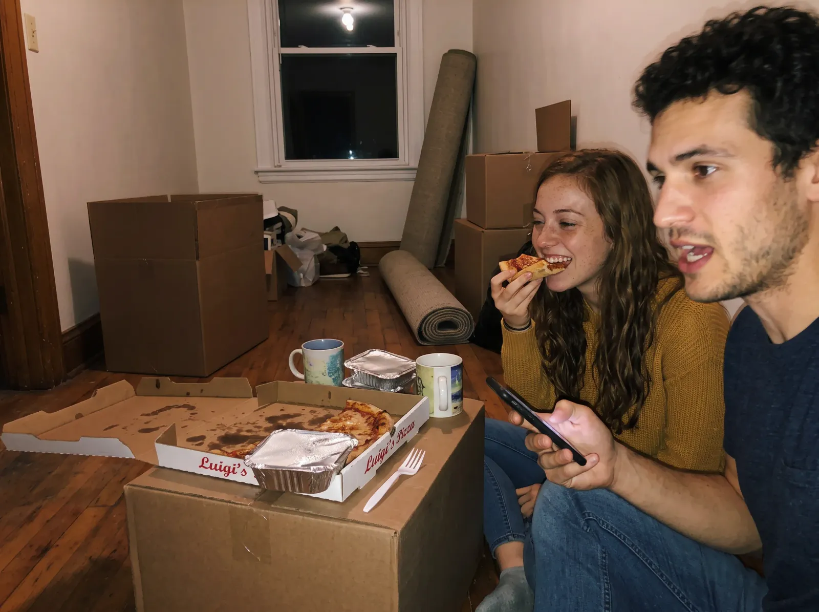 The couple eating pizza off a moving box among unpacked boxes