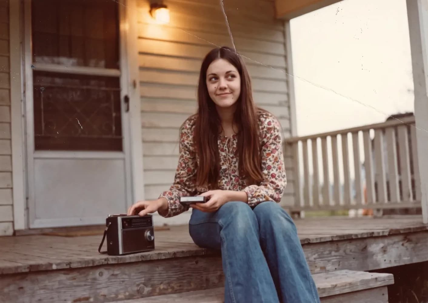 The same girl as a teenager, sitting on a porch step with a radio