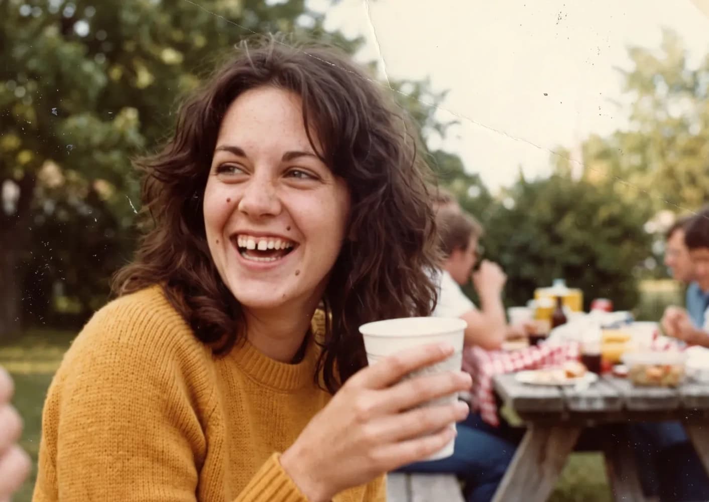 As a young woman, laughing with a cup at a summer picnic