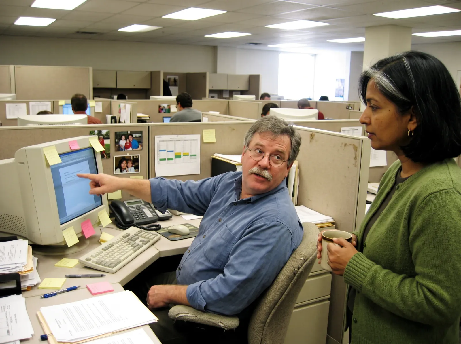 Years later, the same man pointing at his screen for the same colleague